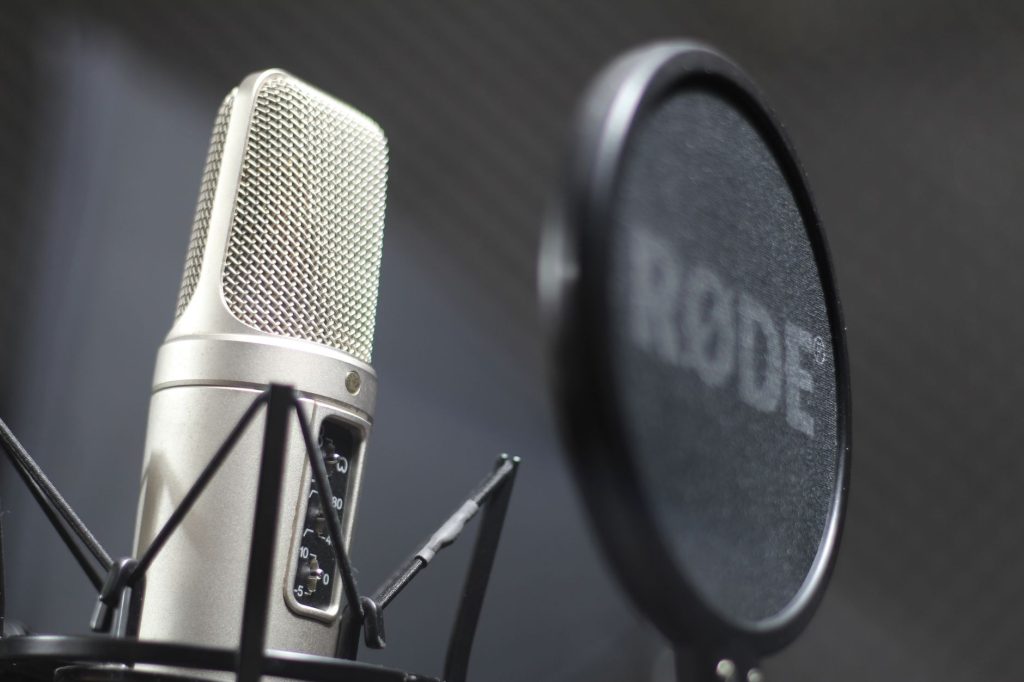 A detailed view of a professional microphone with a pop filter against a gray background.